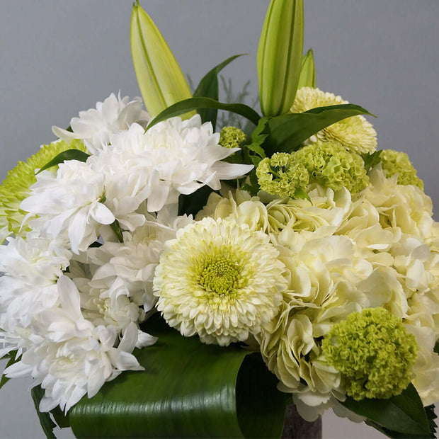 Classic white and green blooms arranged in a clear round vase. Classic flowers like lily and hydrangea make this arrangement  nice and elegant