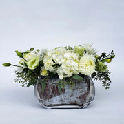 Low rectangular clear vase showcases a captivating combination of white flowers and lush greenery.