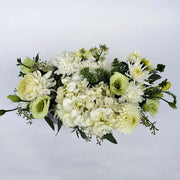 Low rectangular clear vase showcases a captivating combination of white flowers and lush greenery.