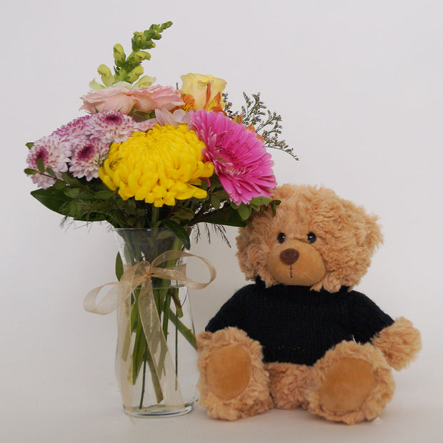Featuring a radiant assortment of seasonal flowers in a small jar and completed with a snuggly plush toy