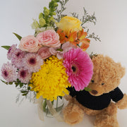 Featuring a radiant assortment of seasonal flowers in a small jar and completed with a snuggly plush toy