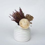 A  mix of dried flowers and sola wood flower in a low white vase. 