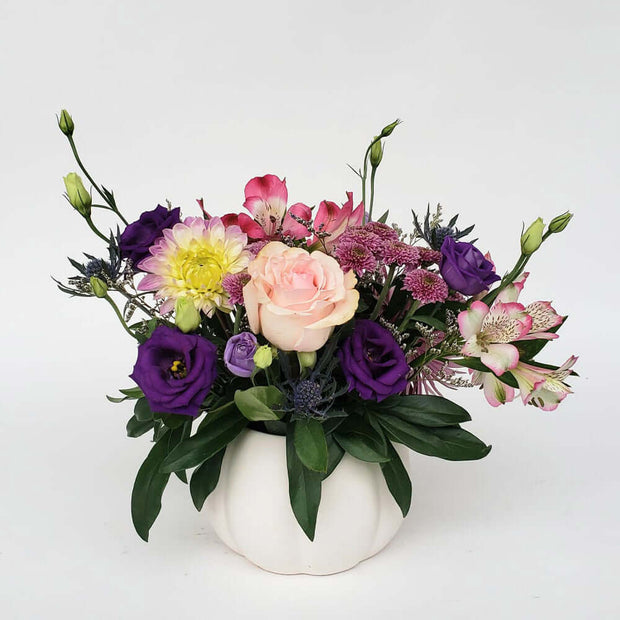 Perfect for those who love pink and purple, this stunning arrangement is set in an elegant white ceramic pumpkin